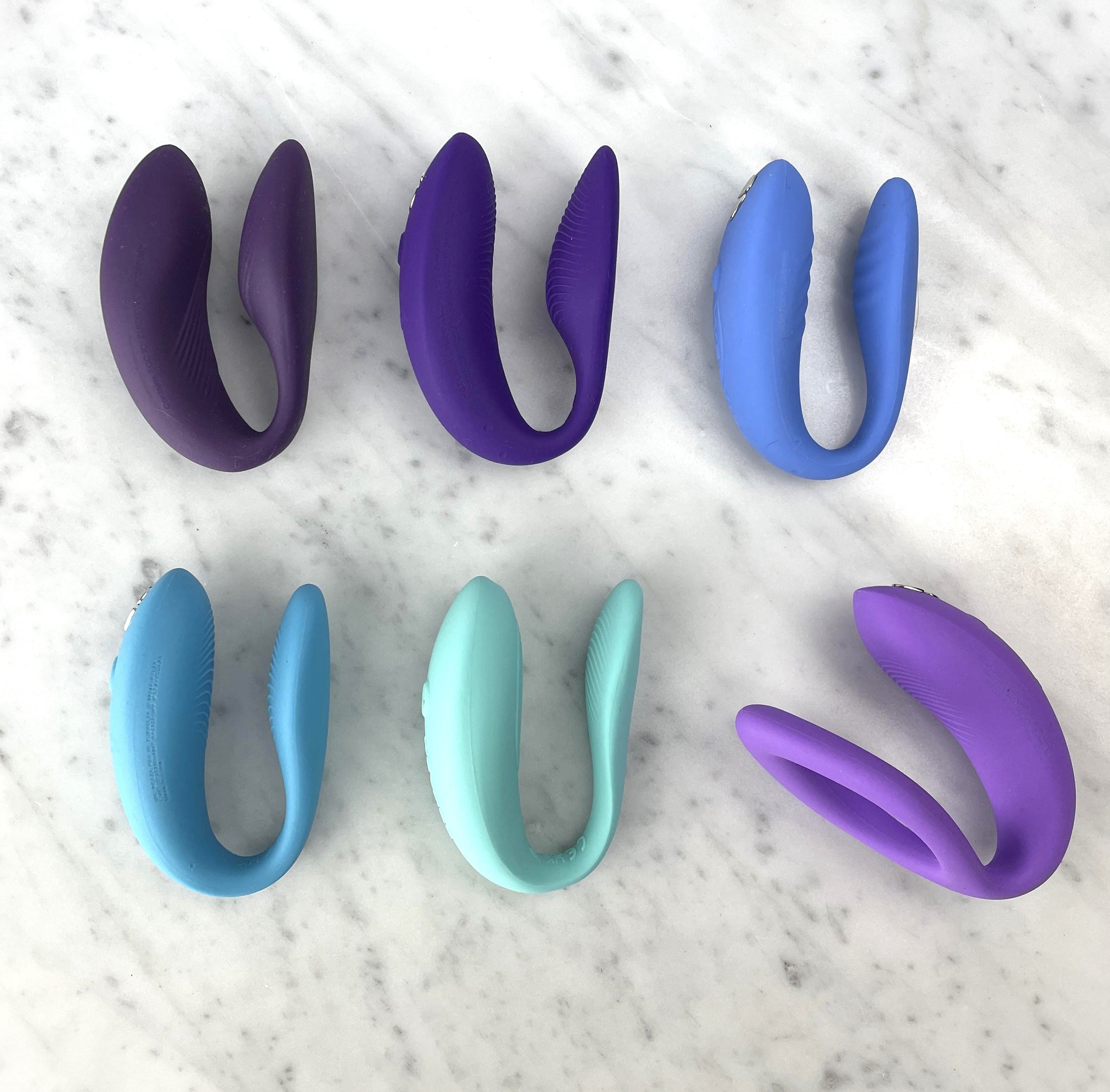 Zes U-vormige We-Vibe koppelvibratoren in paarse, blauwe, mintgroene en lila tinten op marmeren ondergrond