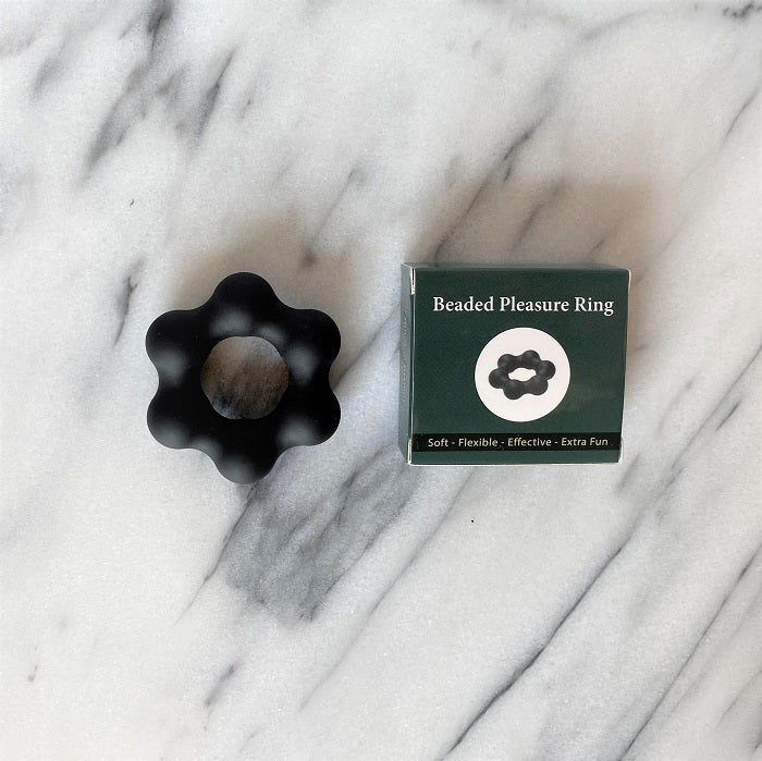 Beaded Pleasure Ring cockring in zwart met bloemvormig ontwerp naast verpakking