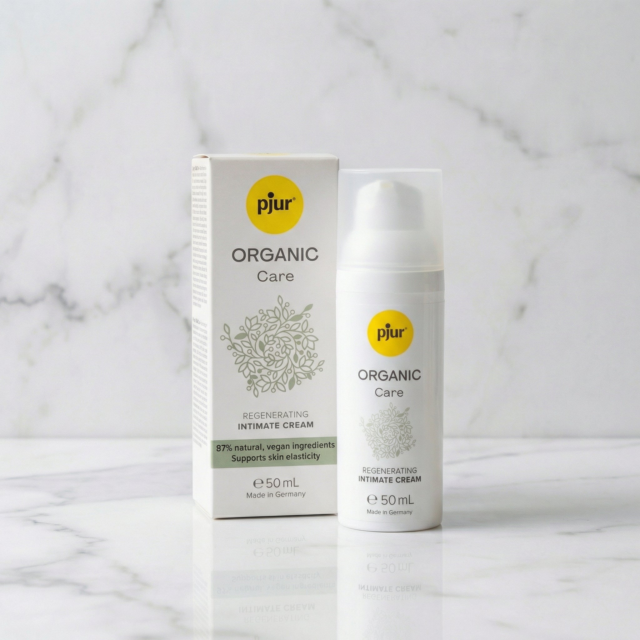 Pjur Organic Care intieme crème 50 ml, witte pompflacon naast kartonnen verpakking met groene bladmotieven