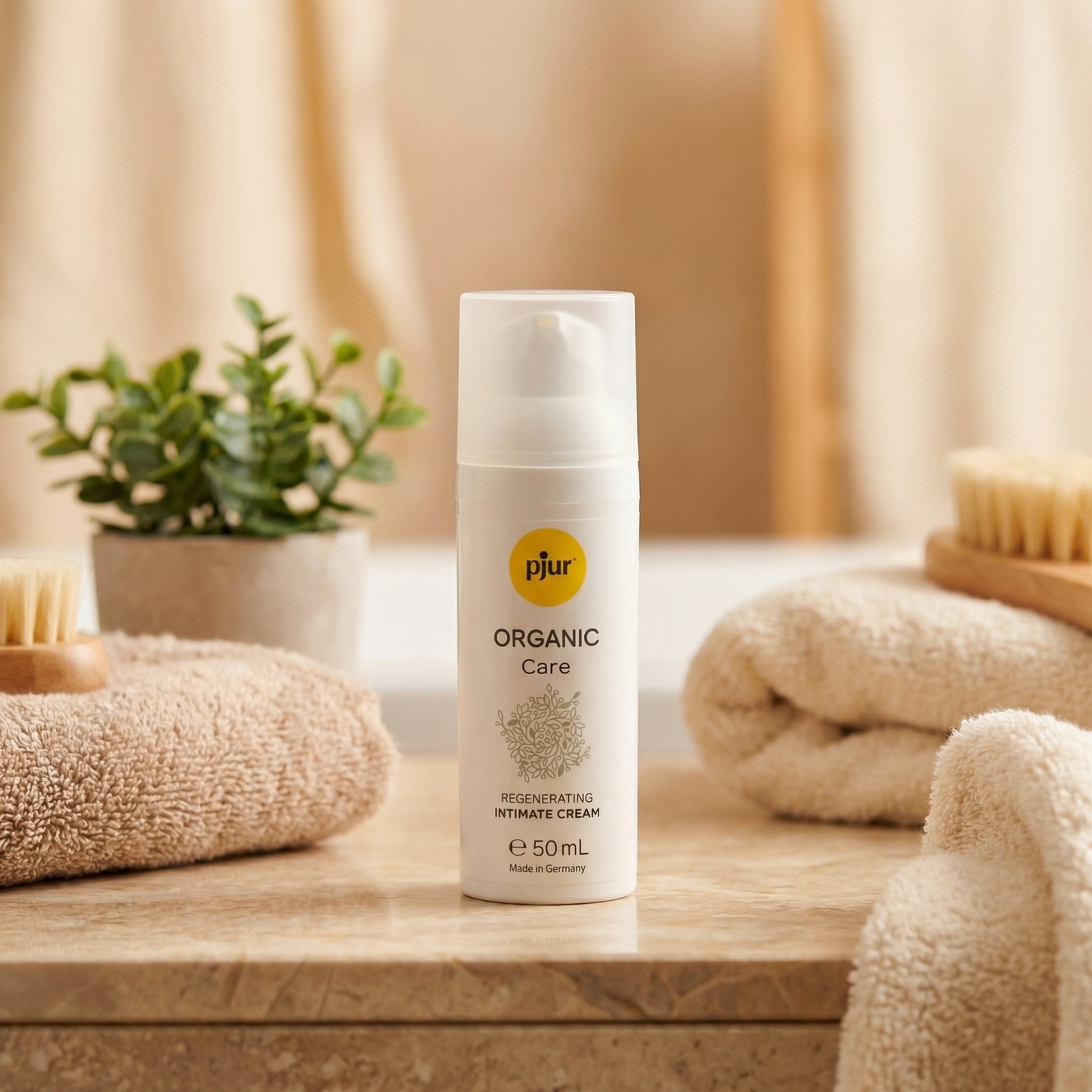 Pjur Organic Care pompflacon in badkamersetting met beige handdoeken, houten borstel en groen plantje