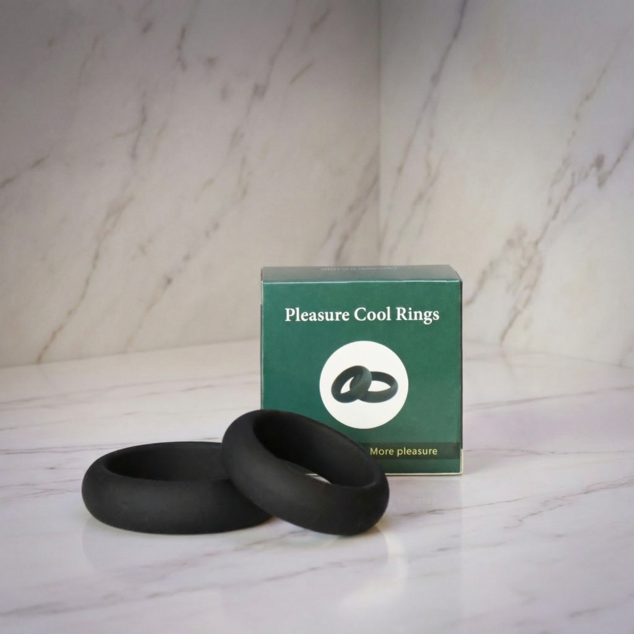 Twee zwarte siliconen cockringen naast groene Pleasure Cool Rings verpakking op marmeren ondergrond