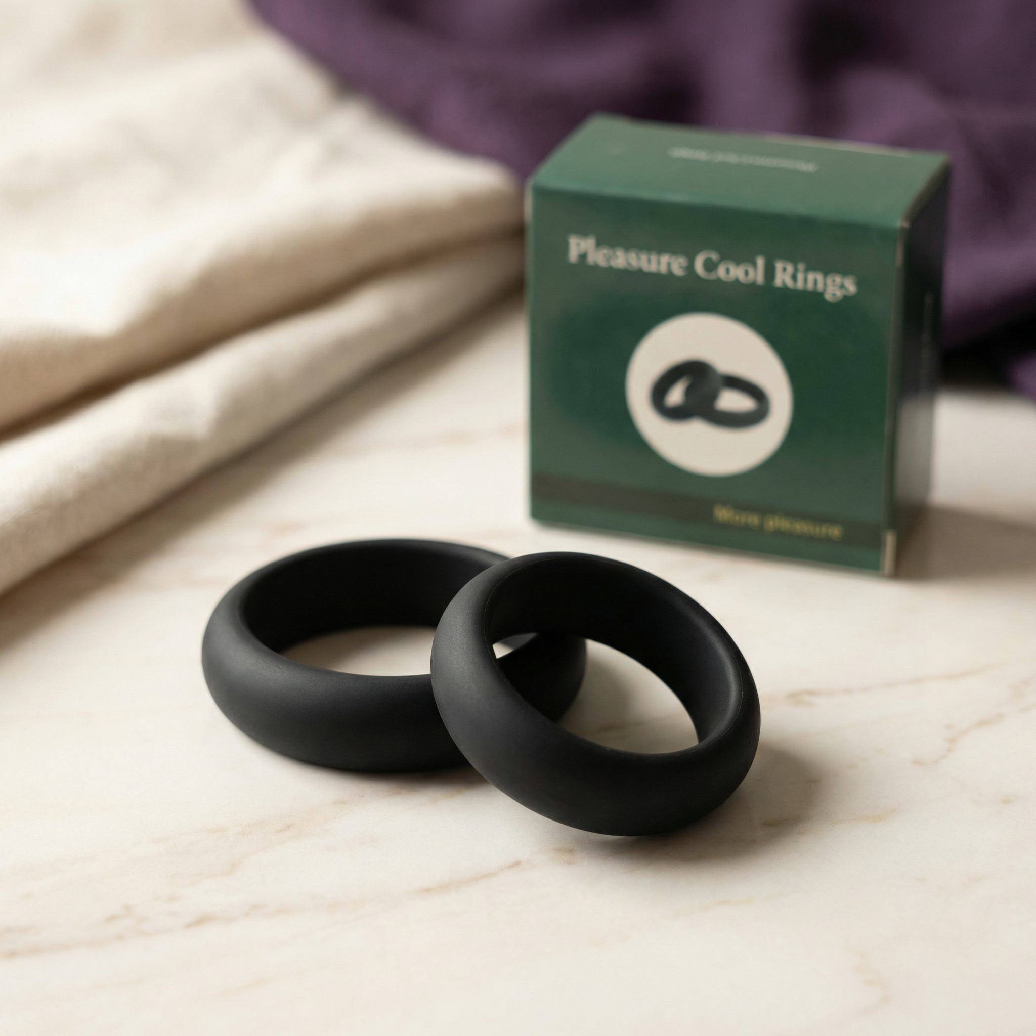 Twee zwarte siliconen cockringen op marmeren blad met groene verpakking en paarse stof op achtergrond