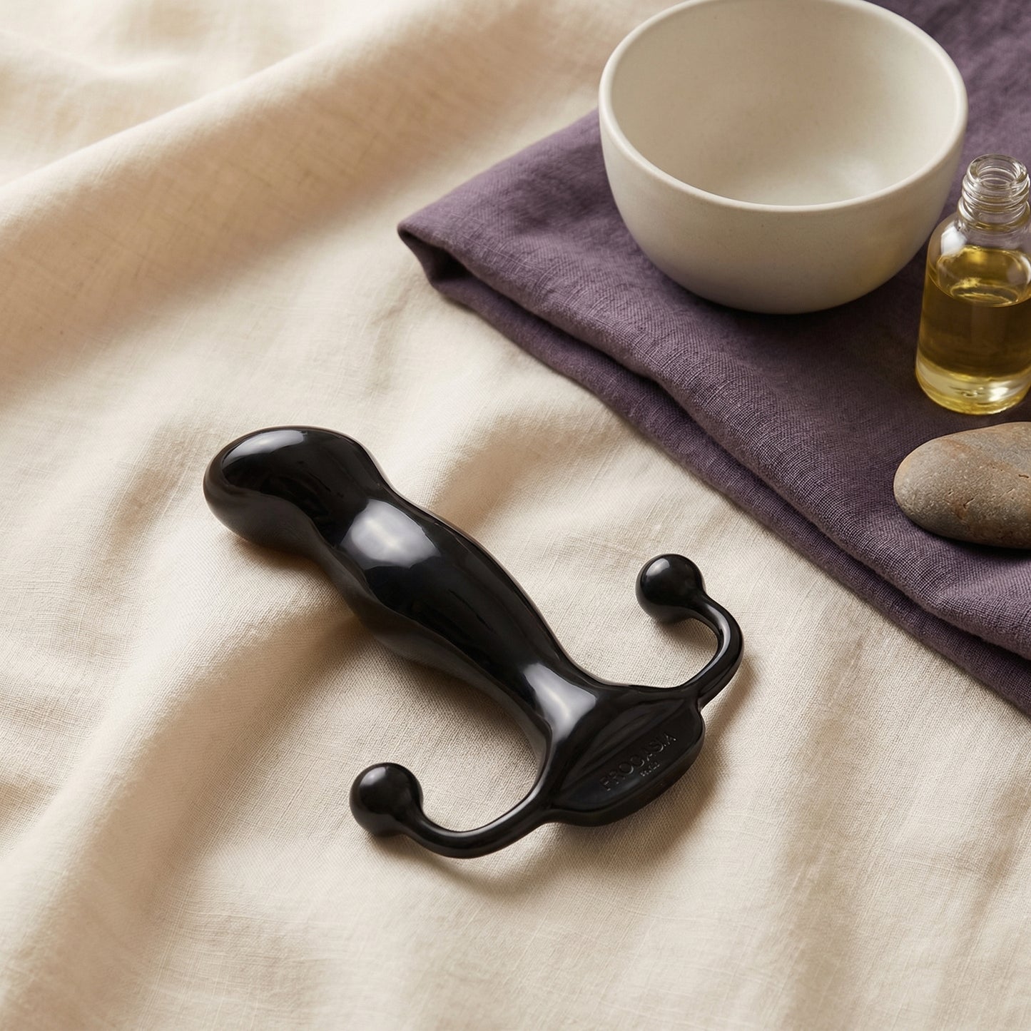 Zwarte glanzende prostaat stimulator met dubbele perineum-armen op linnen stof met olie en stenen