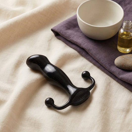 Zwarte glanzende prostaat stimulator met dubbele perineum-armen op linnen stof met olie en stenen