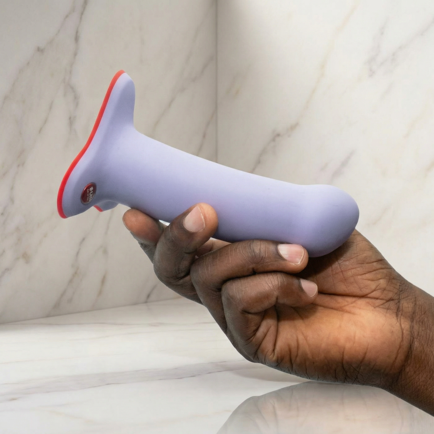 Lavendelkleurige siliconen dildo met rode zuignapbasis en bedieningsknop, in hand