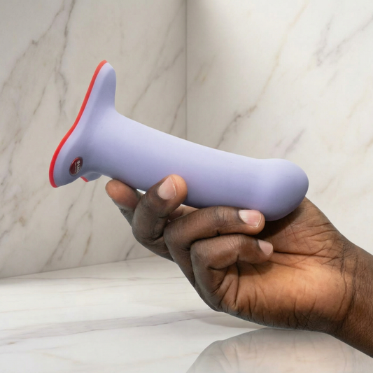 Lavendelkleurige siliconen dildo met rode zuignapbasis en bedieningsknop, in hand