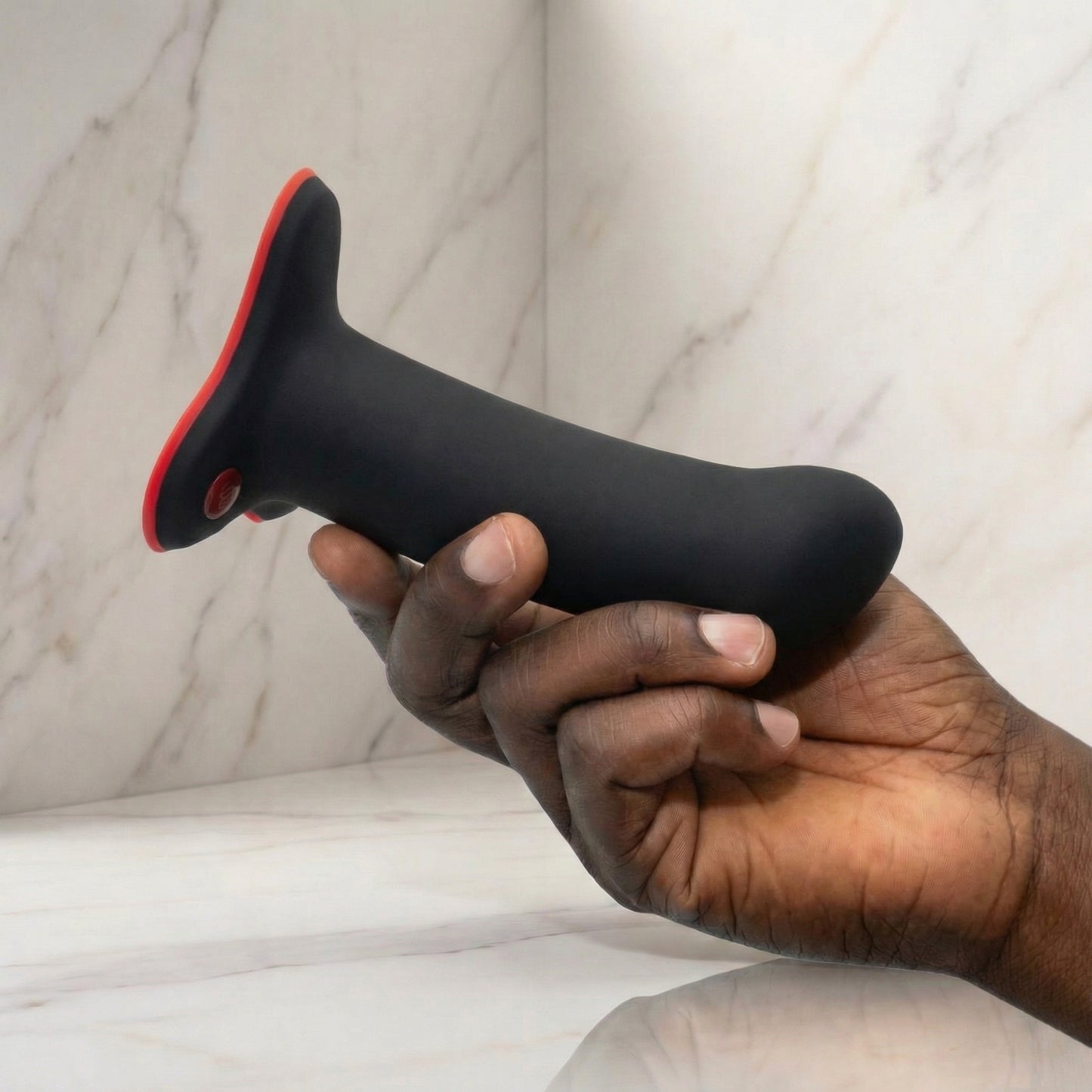 Zwart-rode siliconen dildo met zuignap en bedieningsknop, vastgehouden in hand