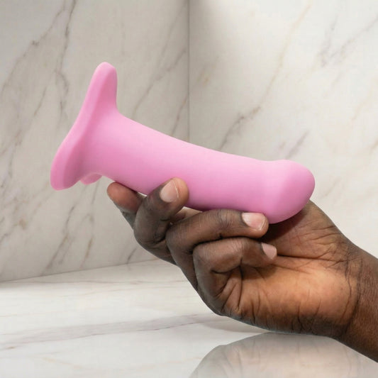Roze siliconen dildo met zuignap basis, vastgehouden in hand tegen marmeren achtergrond
